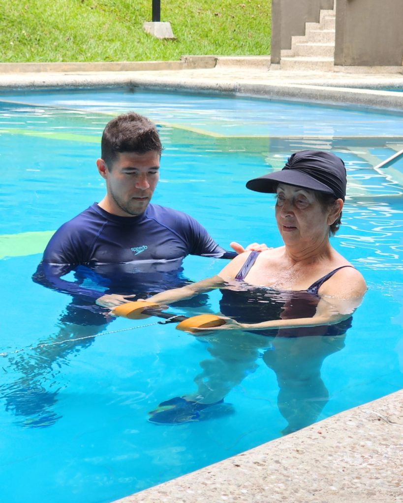 Fisioterapeuta guiando a una paciente en ejercicios de fortalecimiento con pesas acuáticas durante el Plan Fortalece de hidroterapia en Cali.
