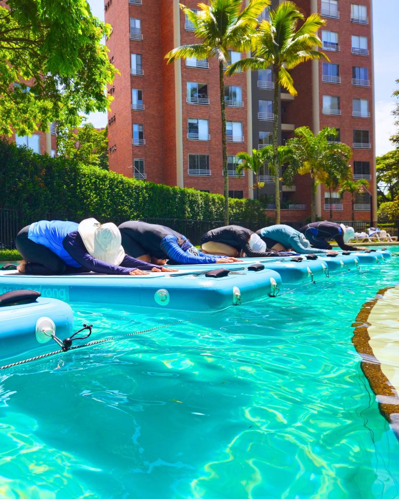 Clase de AquaBOARD Yoga en Cali con AUA FIT. Personas en postura del niño (Balasana) mejorando la flexibilidad y el equilibrio sobre tablas.