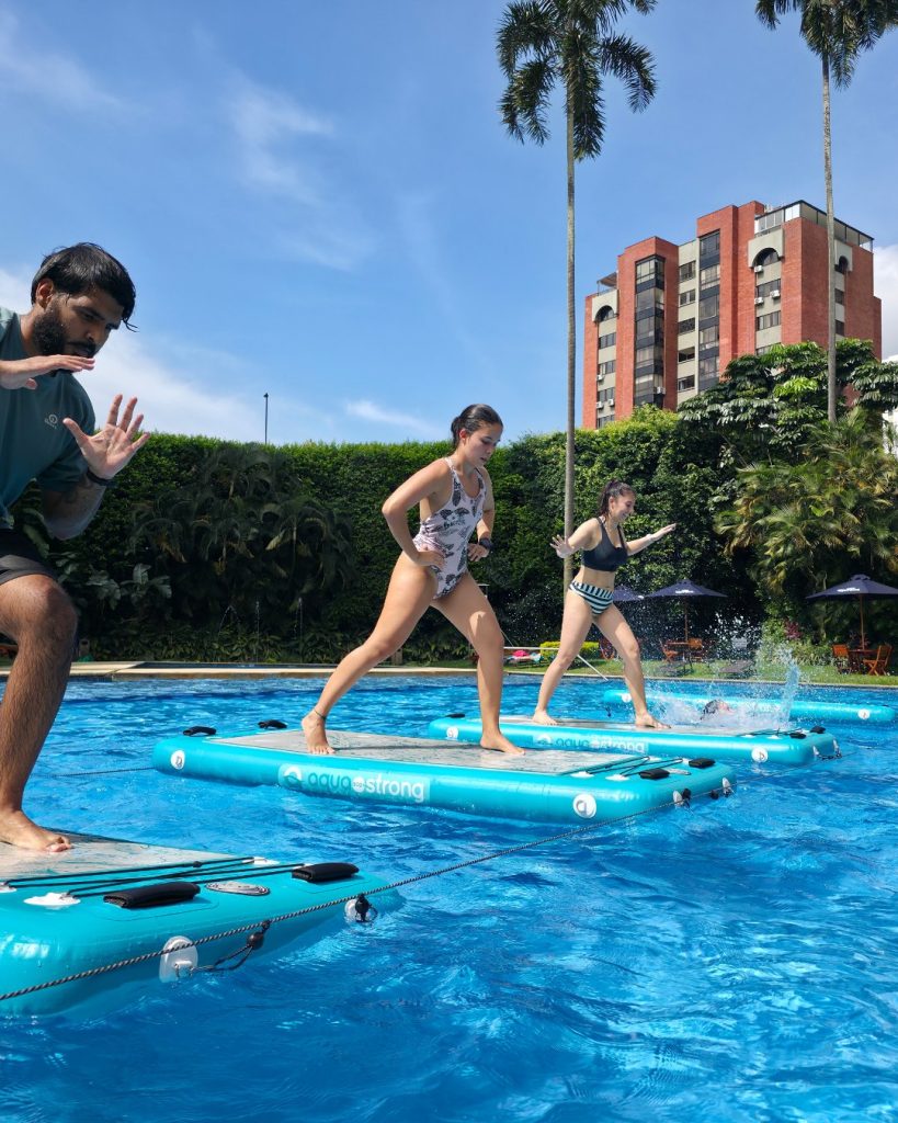 Personas realizando ejercicios de cardio y coordinación sobre tablas AquaStrong en una clase de HIIT acuático al aire libre.