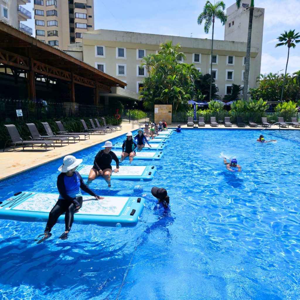 Amplia piscina de lujo en el Hotel Intercontinental Cali con un grupo de personas preparándose para una sesión de AquaBOARD. Entorno exclusivo y santuario de bienestar 5 estrellas operado por AUA FIT.